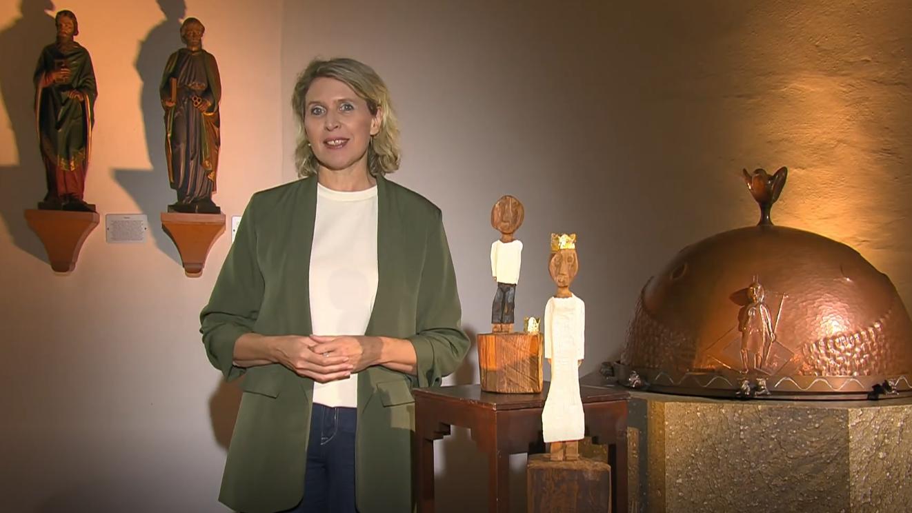 Eine blonde Frau um die 50 Jahre steht neben den Königsfiguren und spricht.