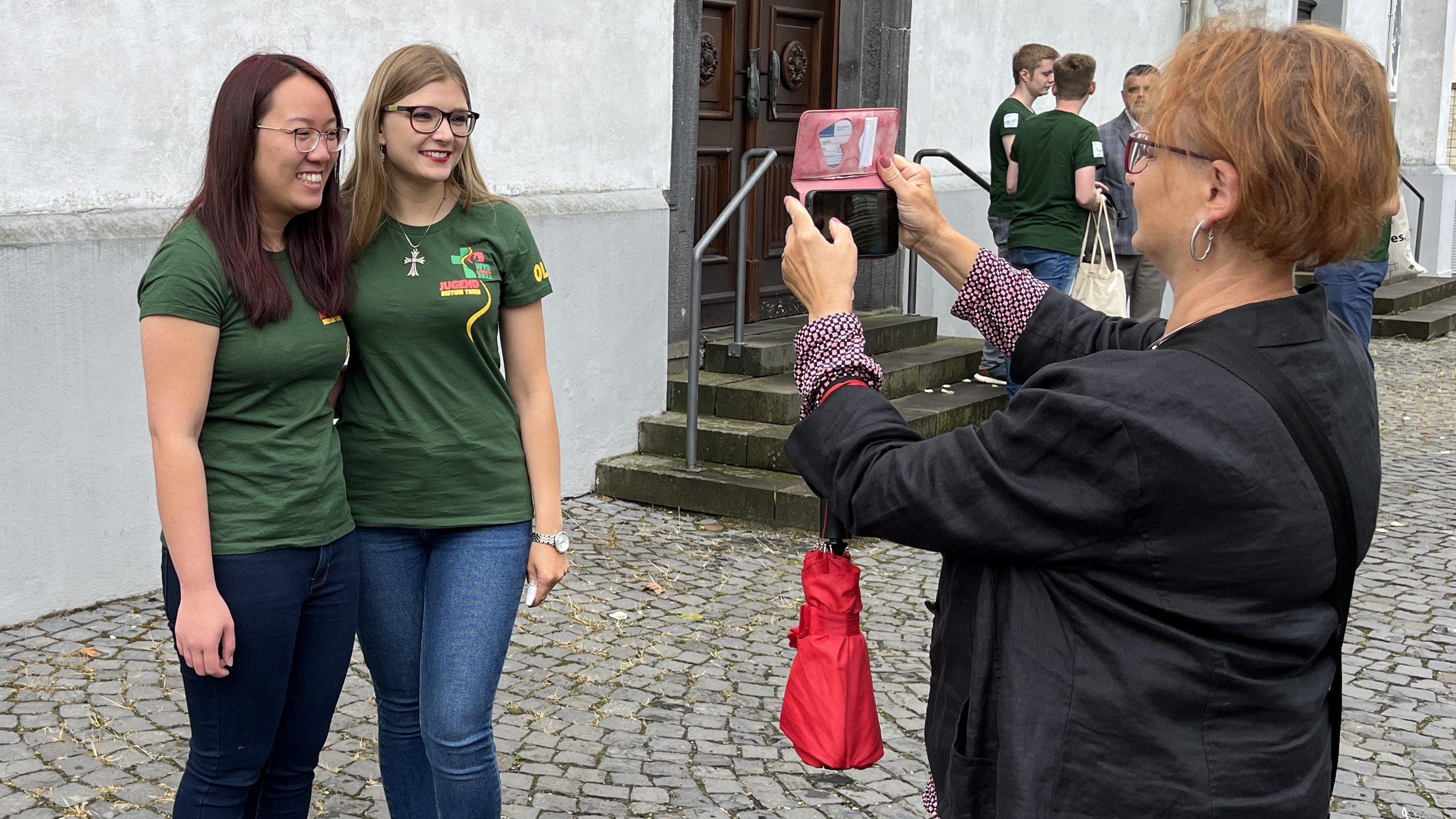Zwei Mädchen stehen vor einer Frau, die mit einem Handy ein Foto macht.