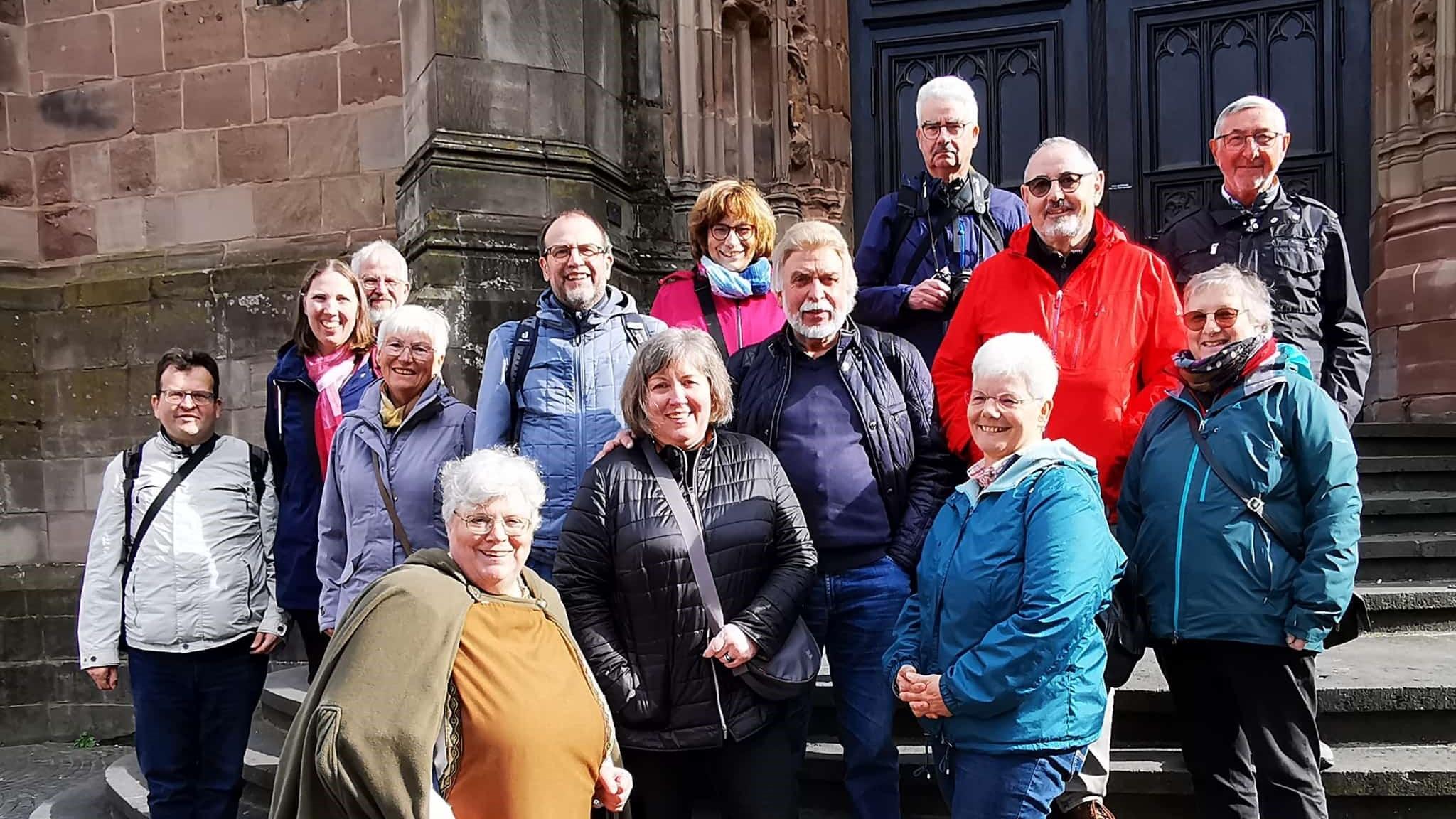 Dreizehn Menschen im fortgesetzten Alter stehen zusammen mit einer Pilgerführerin auf den Stufen zur Basilika.
