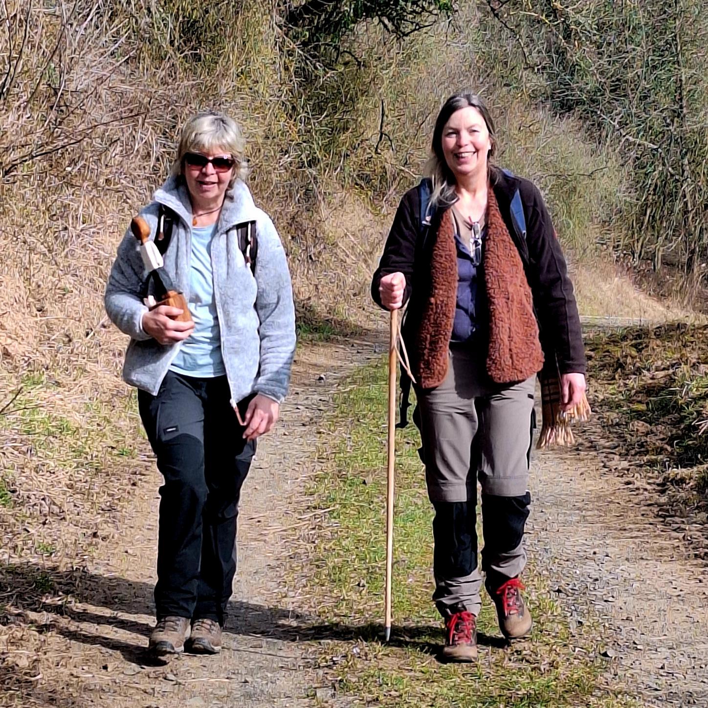 Zwei Frau unterschiedlichen Alters gehen nebeneinander auf einem Feldweg. Die ältere trägt die kleine Köngisfigur in ihrer rechten Hand.