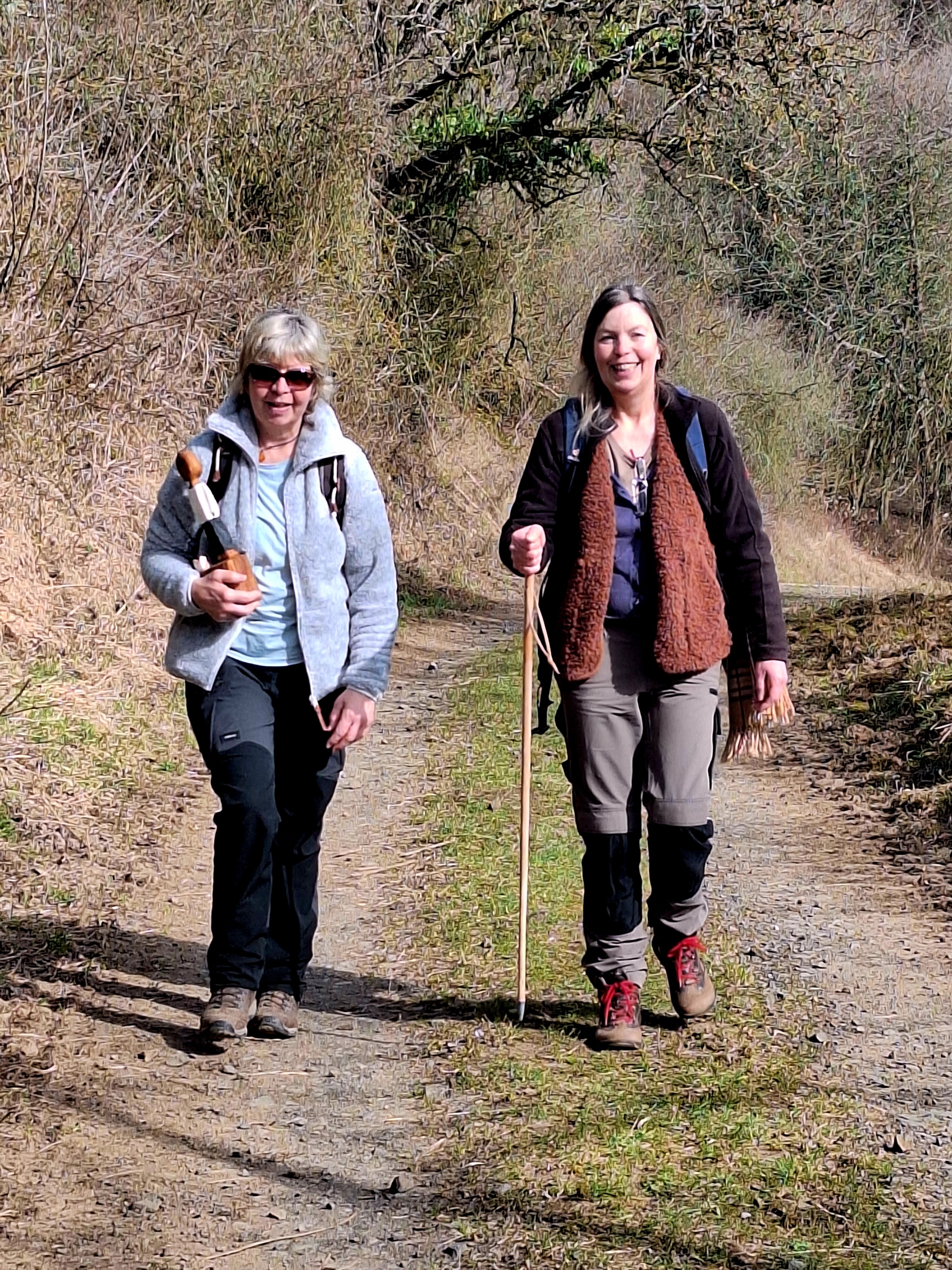 Zwei Frau unterschiedlichen Alters gehen nebeneinander auf einem Feldweg. Die ältere trägt die kleine Köngisfigur in ihrer rechten Hand.