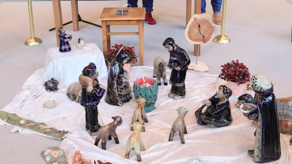 Vor dem Altarraum in Heilig Kreuz Neuwied stehen auf einem Tisch viele kleine Tonbecher, davor auf einem Hocker ein Stern, davor eine Krippe aus glasiertem Ton auf einem weißen Tuch.