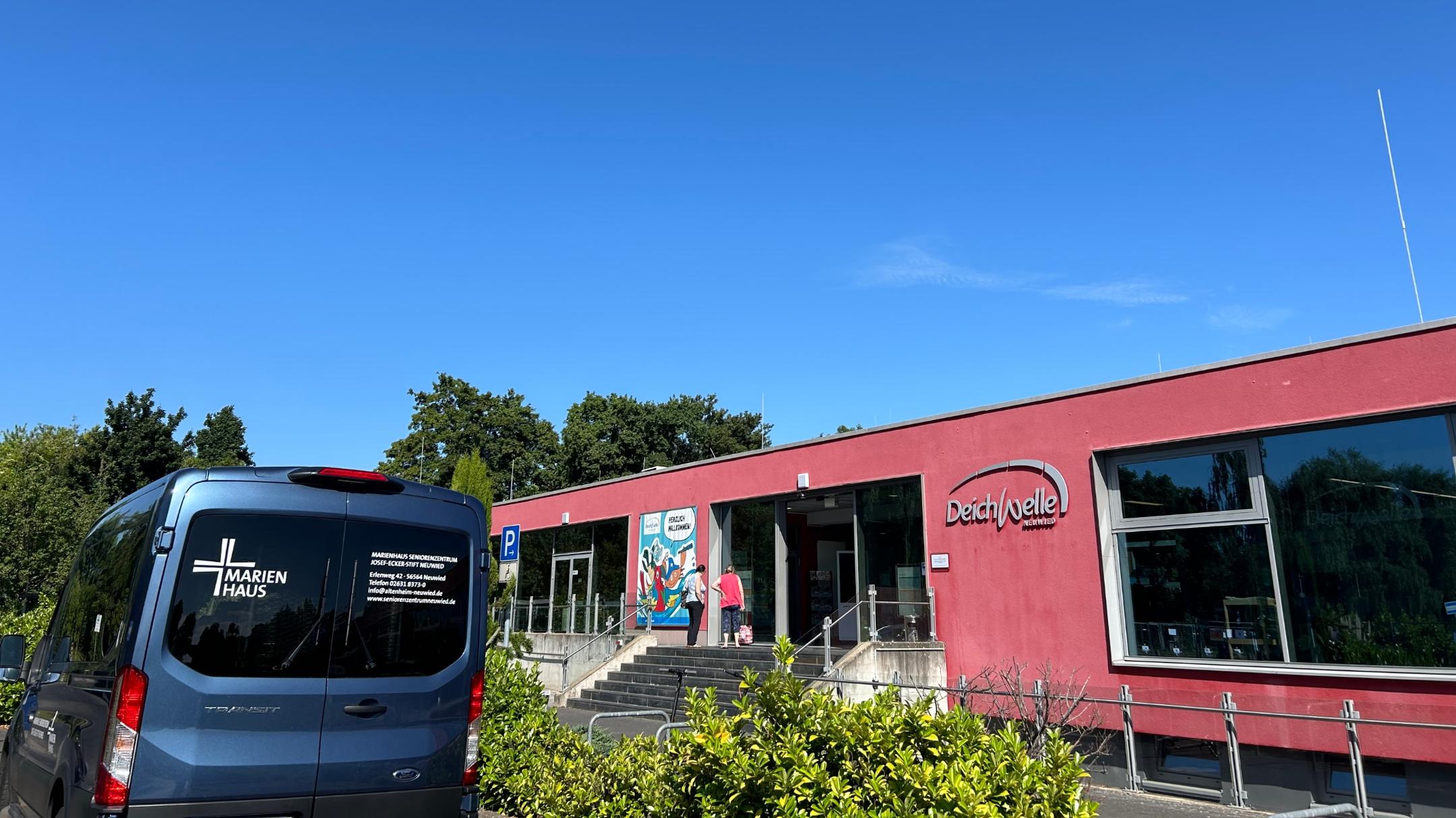 Der einrichtungseigene blaue Kleinbus steht vor dem Eingang des Freibades.