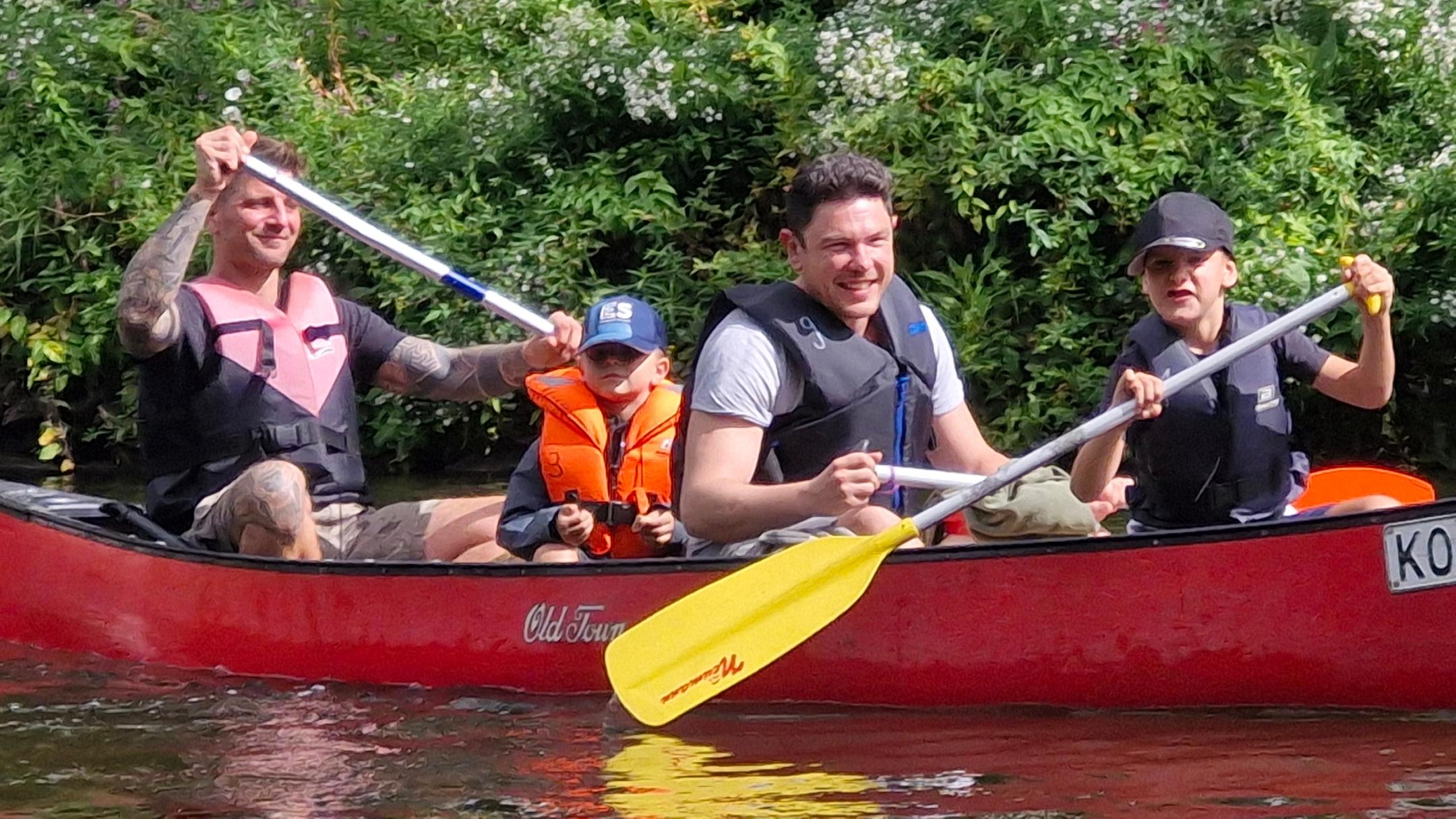 Zwei Väter mit ihren beiden Kindern paddeln in einem roten Boot auf der Lahn.