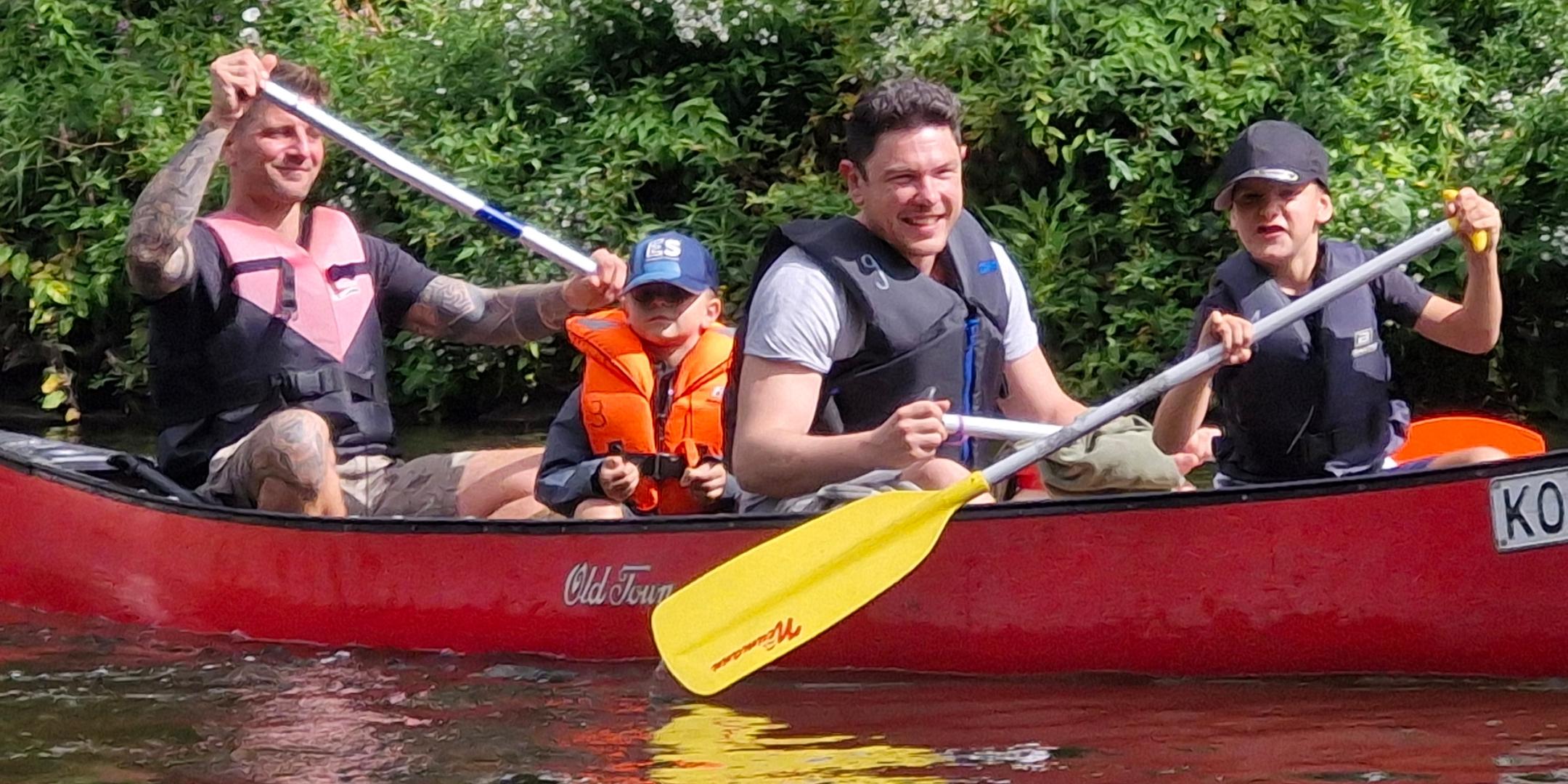 Zwei Väter mit ihren beiden Kindern paddeln in einem roten Boot auf der Lahn.