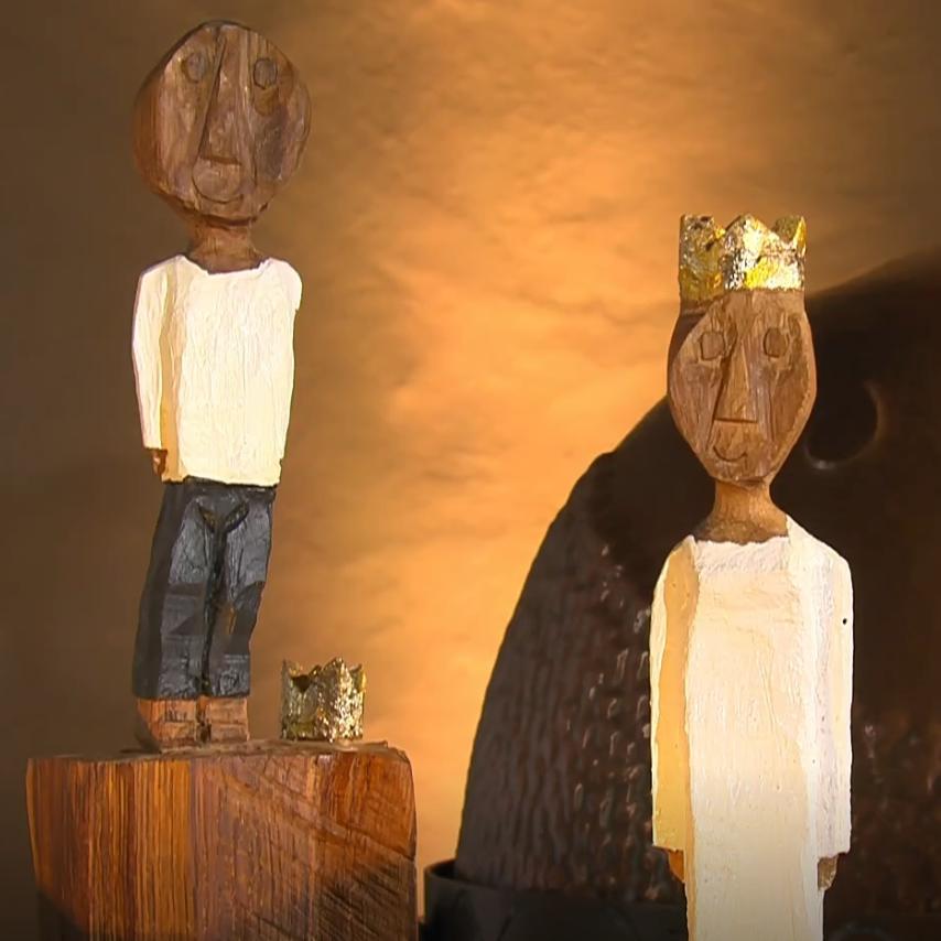 Der kleine König steht etwas erhöht hinter der großen Königin. Der Hintergrund ist in einem warmen Geld beleuchtet.