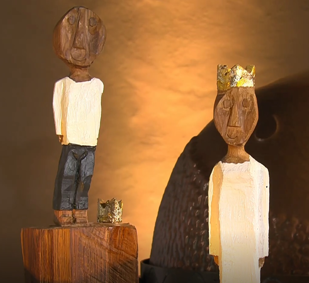 Der kleine König steht etwas erhöht hinter der großen Königin. Der Hintergrund ist in einem warmen Geld beleuchtet.