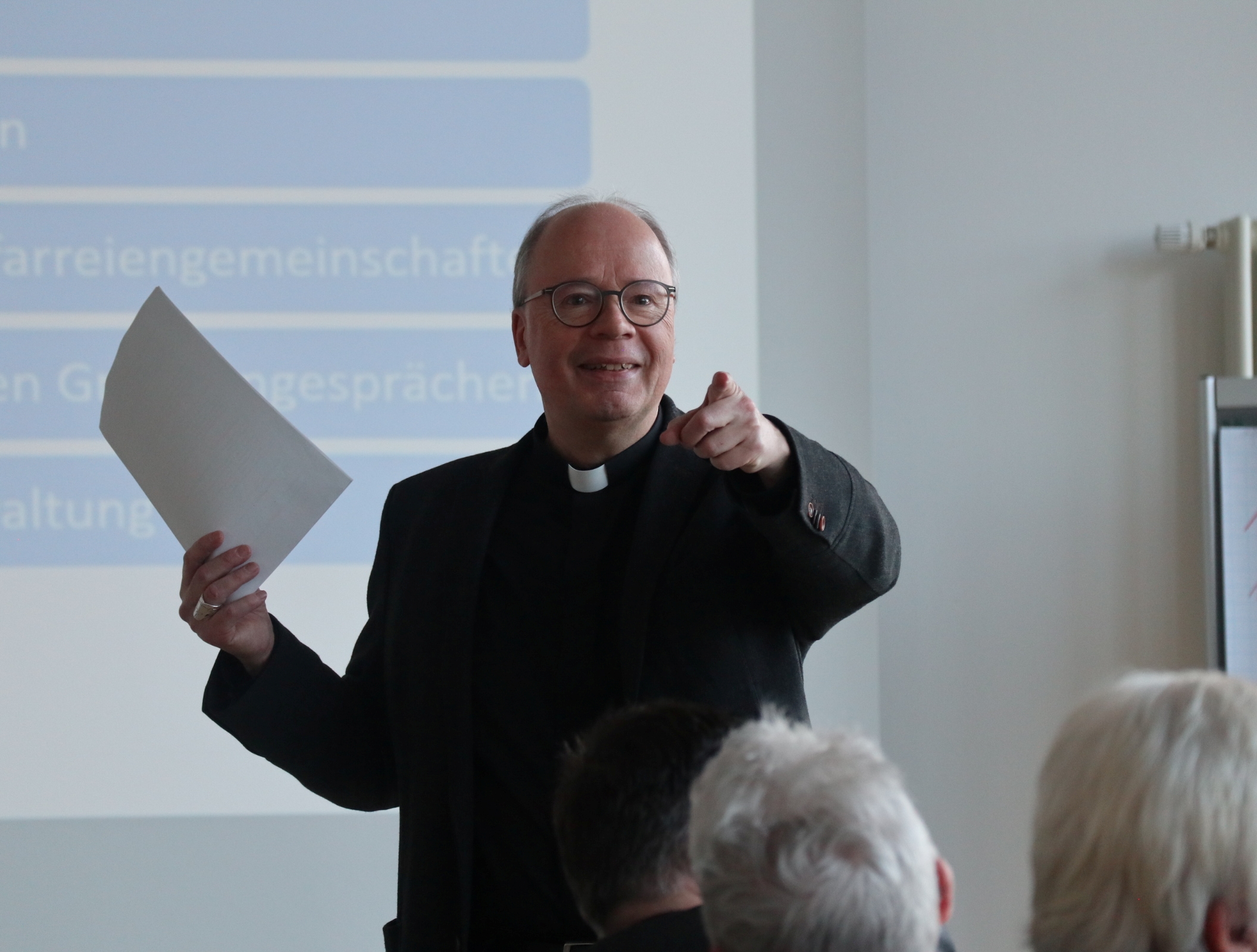 Bischof Ackermann steht vor den Teilnehmenden und zeigt begeistert in die Runde.
