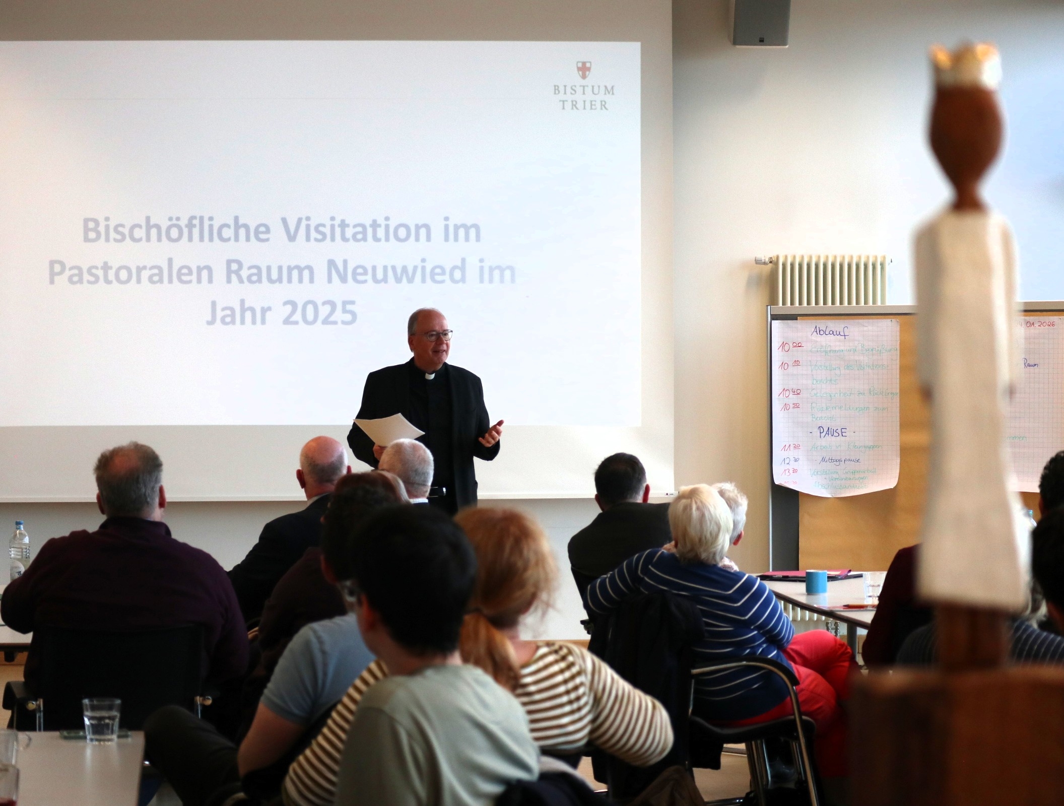 Bischof Ackermann steht erzählend vor den sitzenden Teilnehmenden. Eine der Königsfiguren schaut zu.