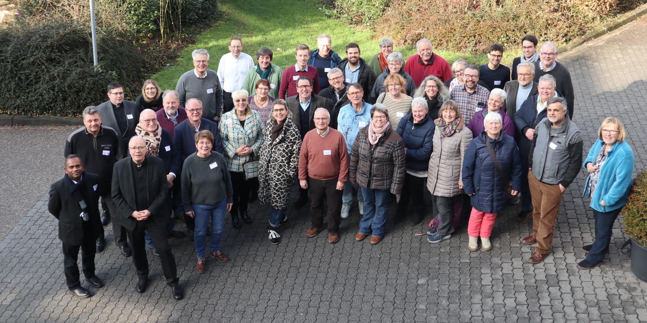 Die Teilnehmenden - zum Teil in Winterjacken - stehen zusammen mit Bischof Ackermann gut gelaunt als Gruppe zusammen und schauen zur Fotografin hinauf.