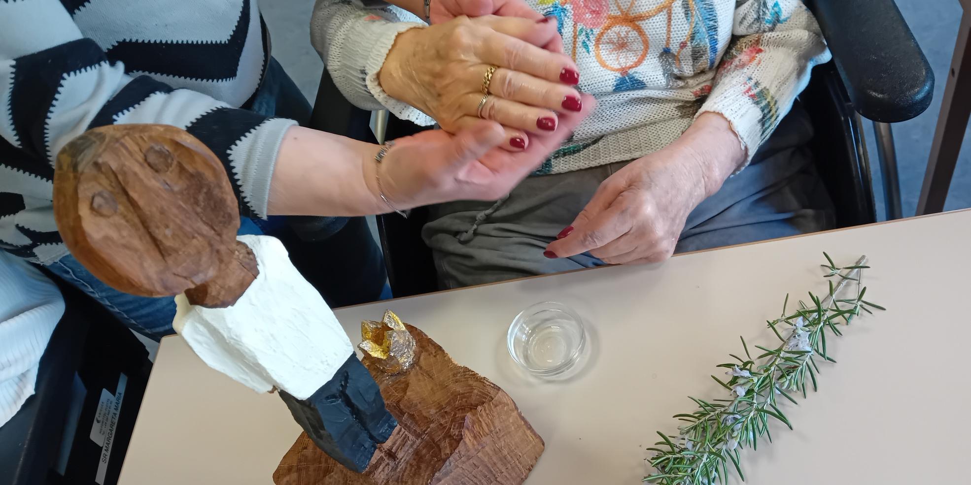 Die kleine Königsfigur steht auf einem Tisch. Daneben werden alte Hände von jüngeren gesalbt.