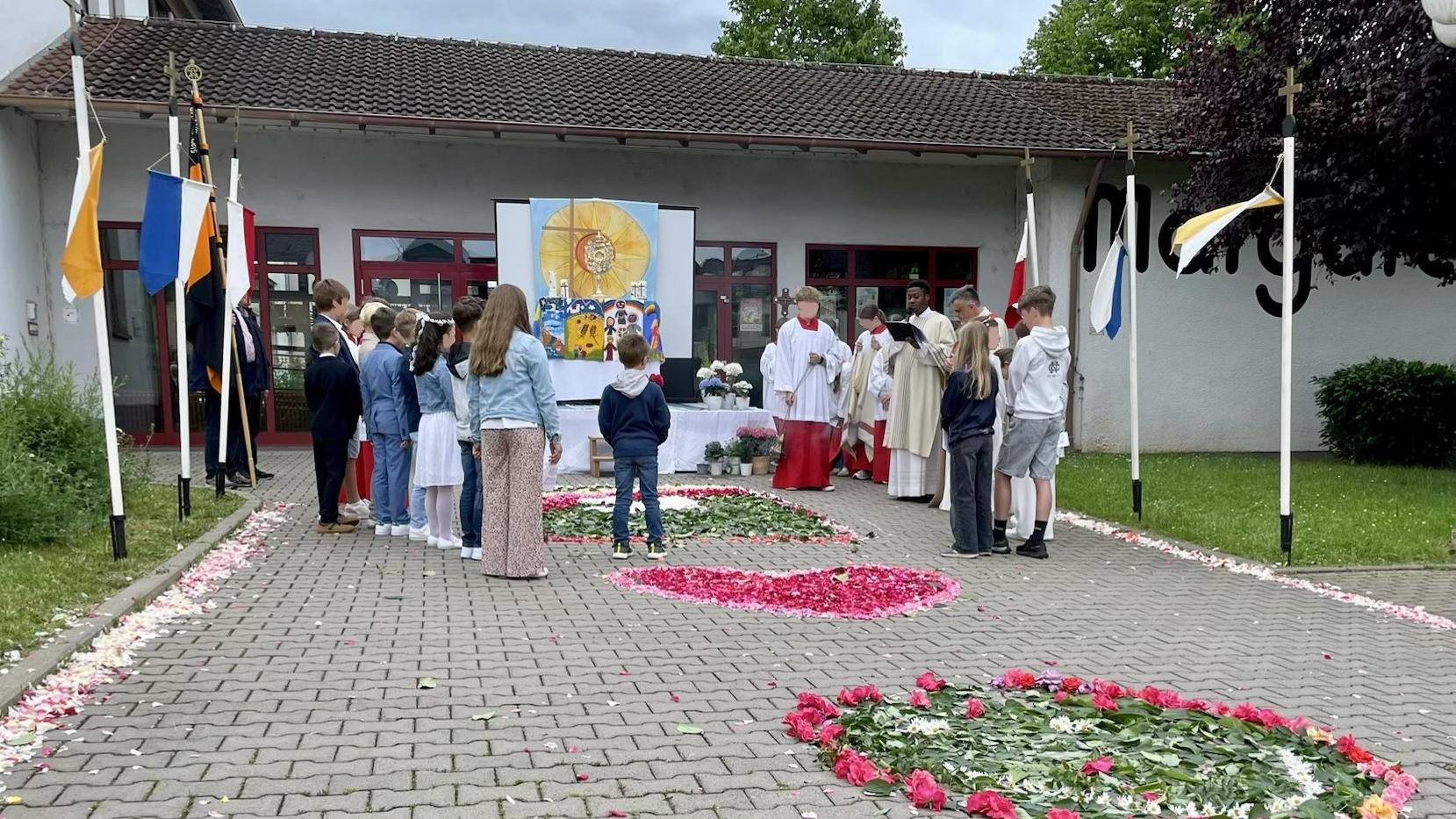 An der gestalteten Station haben sich die Kommunionkinder, die Messdiener*innen sowie die beiden Priester versammelt.