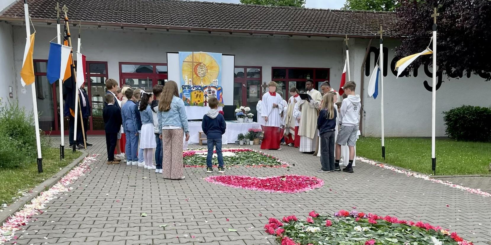 An der gestalteten Station haben sich die Kommunionkinder, die Messdiener*innen sowie die beiden Priester versammelt.