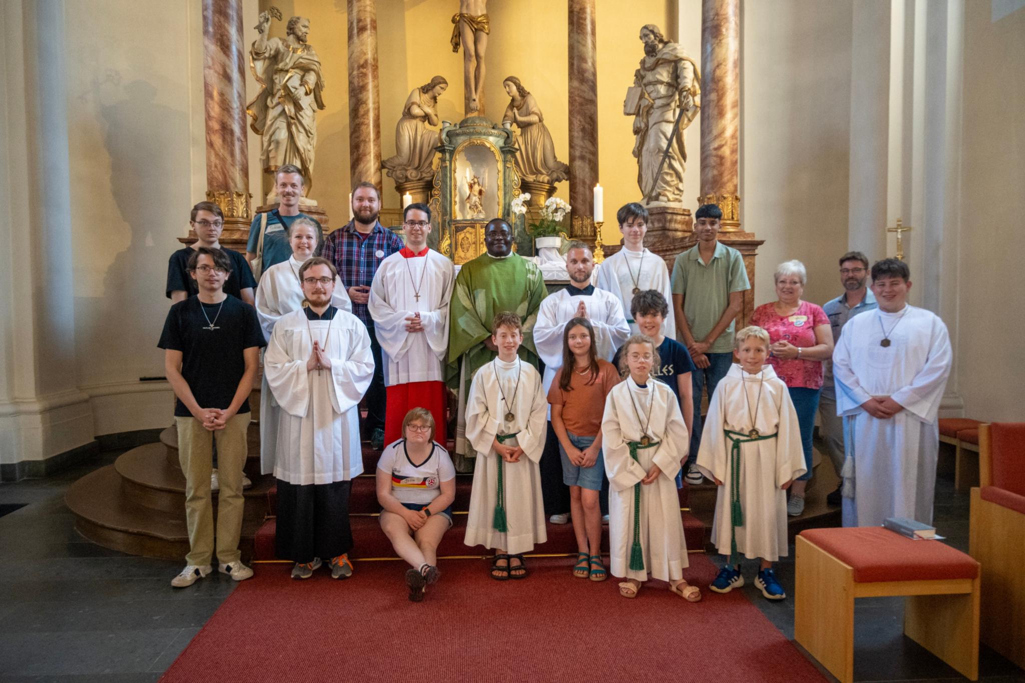 Die Teilnehmenden stehen, teils in Ministrant*innen-Kleidung, gemeinsam mit Pater Magnus auf den Stufen zum Hochaltar in der Pfarrkirche in Bad Hönningen.