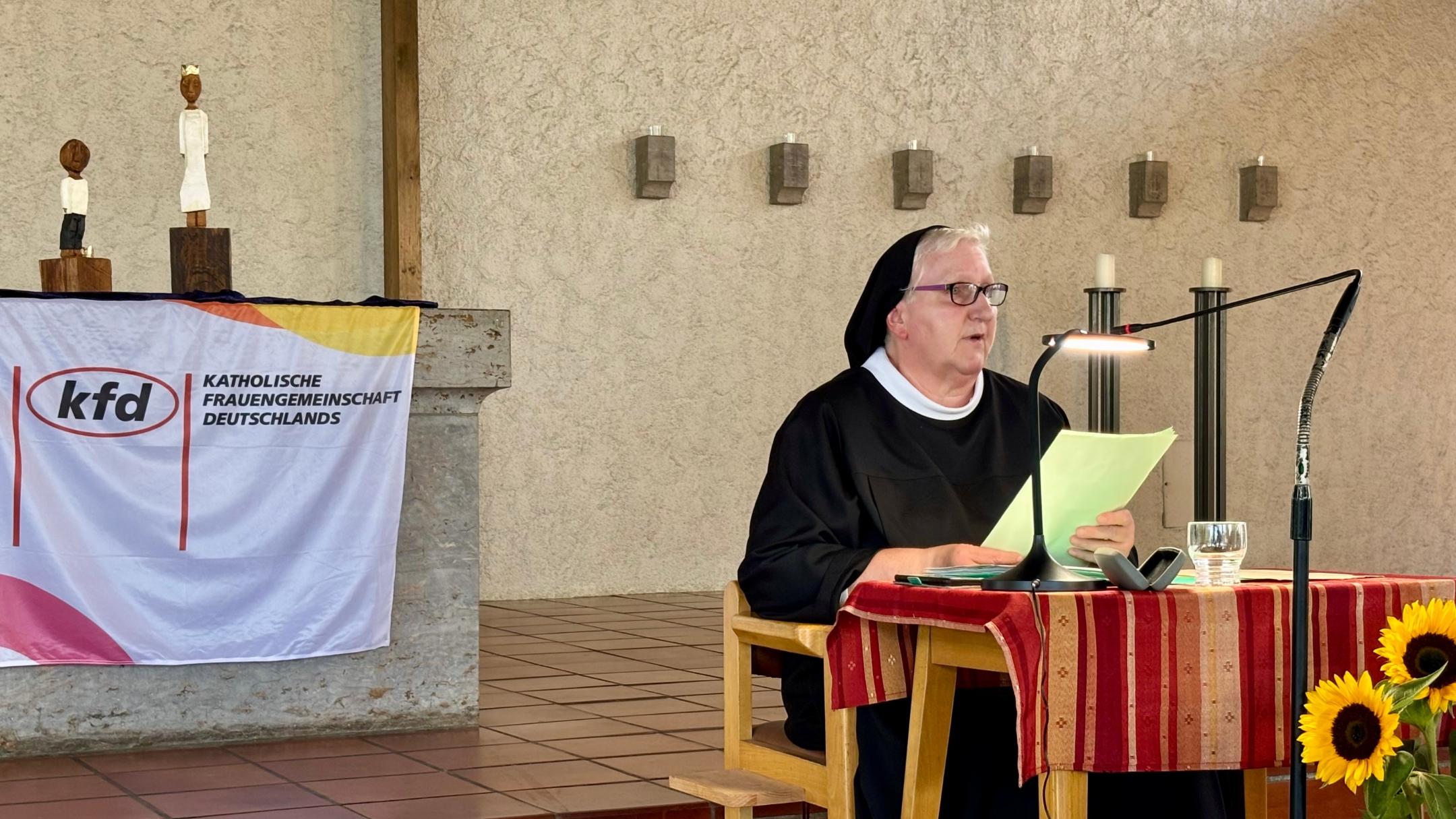 Sr. Philippa Rath, in Ordenstracht, sitzt an einem kleinen Tisch und spricht ins Mikrofon. Hinter ihr, auf dem Altar, stehen den Königsfiguren des Pastoralen Raumes Neuwied.