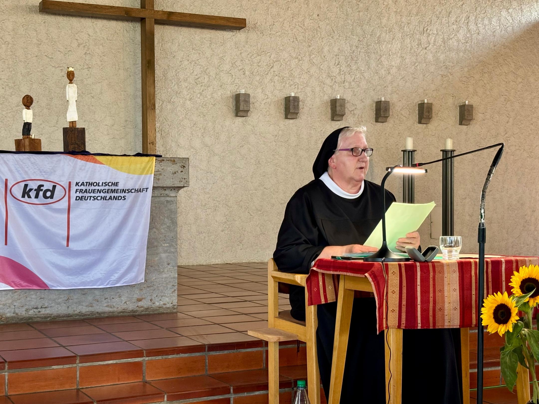 Sr. Philippa Rath, in Ordenstracht, sitzt an einem kleinen Tisch und spricht ins Mikrofon. Hinter ihr, auf dem Altar, stehen den Königsfiguren des Pastoralen Raumes Neuwied.