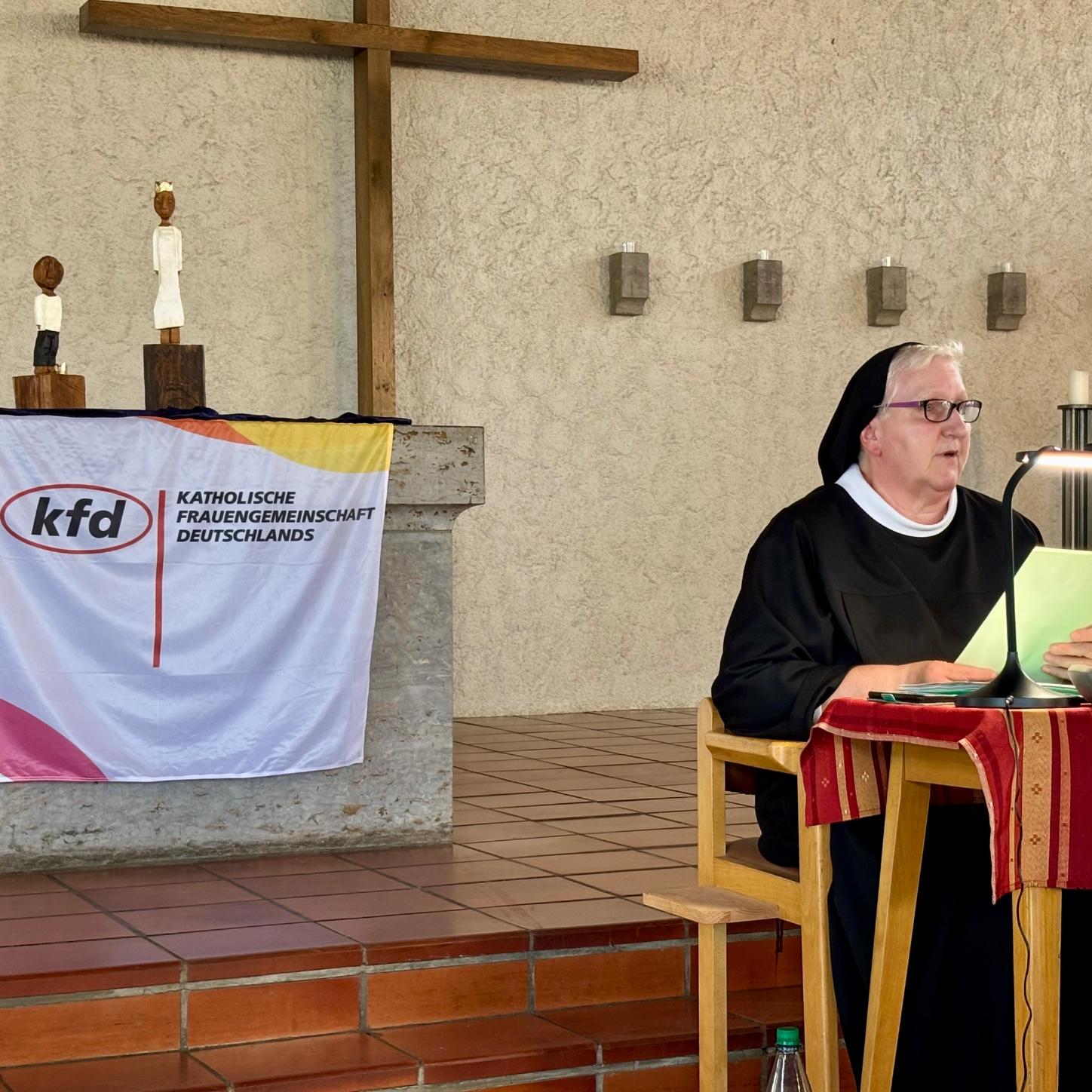Sr. Philippa Rath, in Ordenstracht, sitzt an einem kleinen Tisch und spricht ins Mikrofon. Hinter ihr, auf dem Altar, stehen den Königsfiguren des Pastoralen Raumes Neuwied.