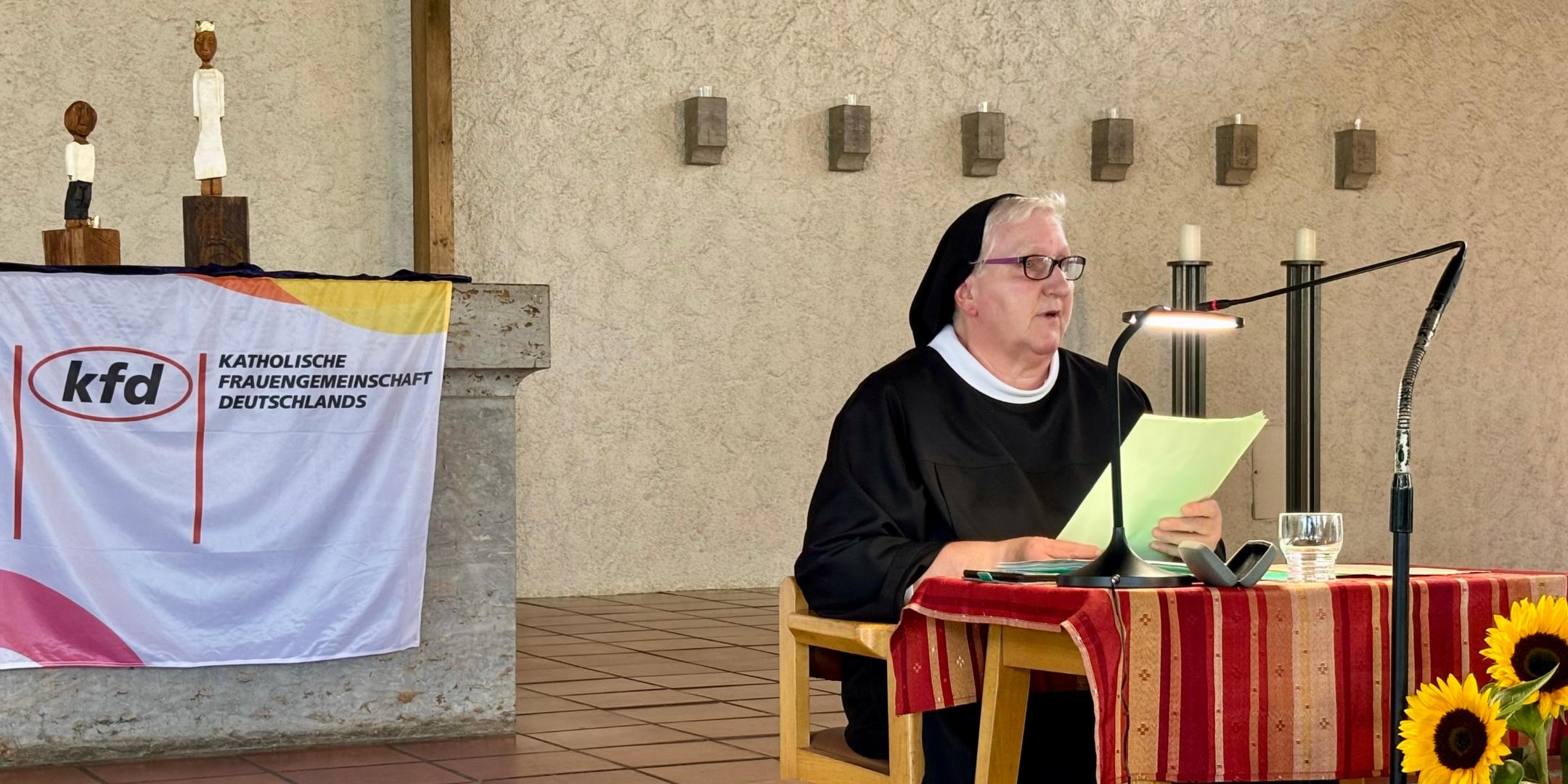 Sr. Philippa Rath, in Ordenstracht, sitzt an einem kleinen Tisch und spricht ins Mikrofon. Hinter ihr, auf dem Altar, stehen den Königsfiguren des Pastoralen Raumes Neuwied.