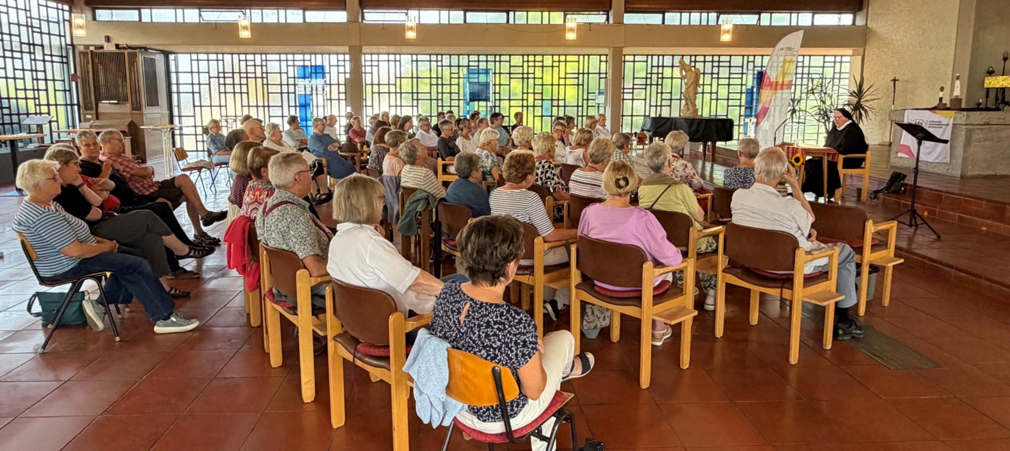 Etwa 70 Personen sitzen auf Stühlen im Halbkreis und lauschen Sr. Philippa Rath in der katholischen Kirche in Feldkirchen.
