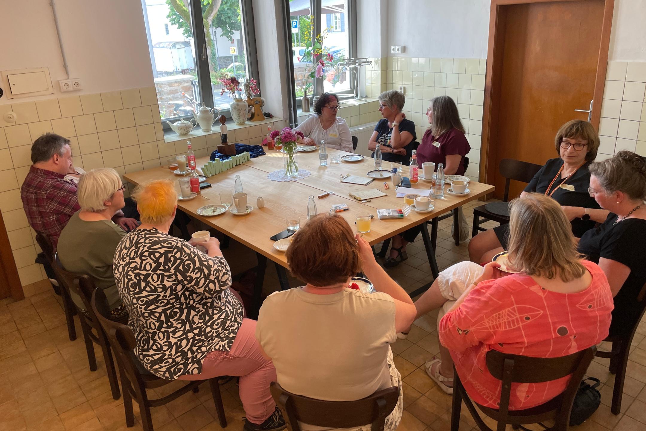 10 Frauen und ein Mann sitzen um einen gedeckten Tisch.