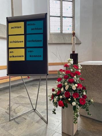 Hinter einer Flipchart mit gegensätzlichen Wortpaaren steht die Königin auf dem Altar.