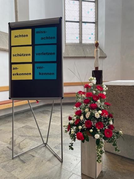 Hinter einer Flipchart mit gegensätzlichen Wortpaaren steht die Königin auf dem Altar.