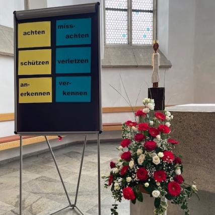 Hinter einer Flipchart mit gegensätzlichen Wortpaaren steht die Königin auf dem Altar.