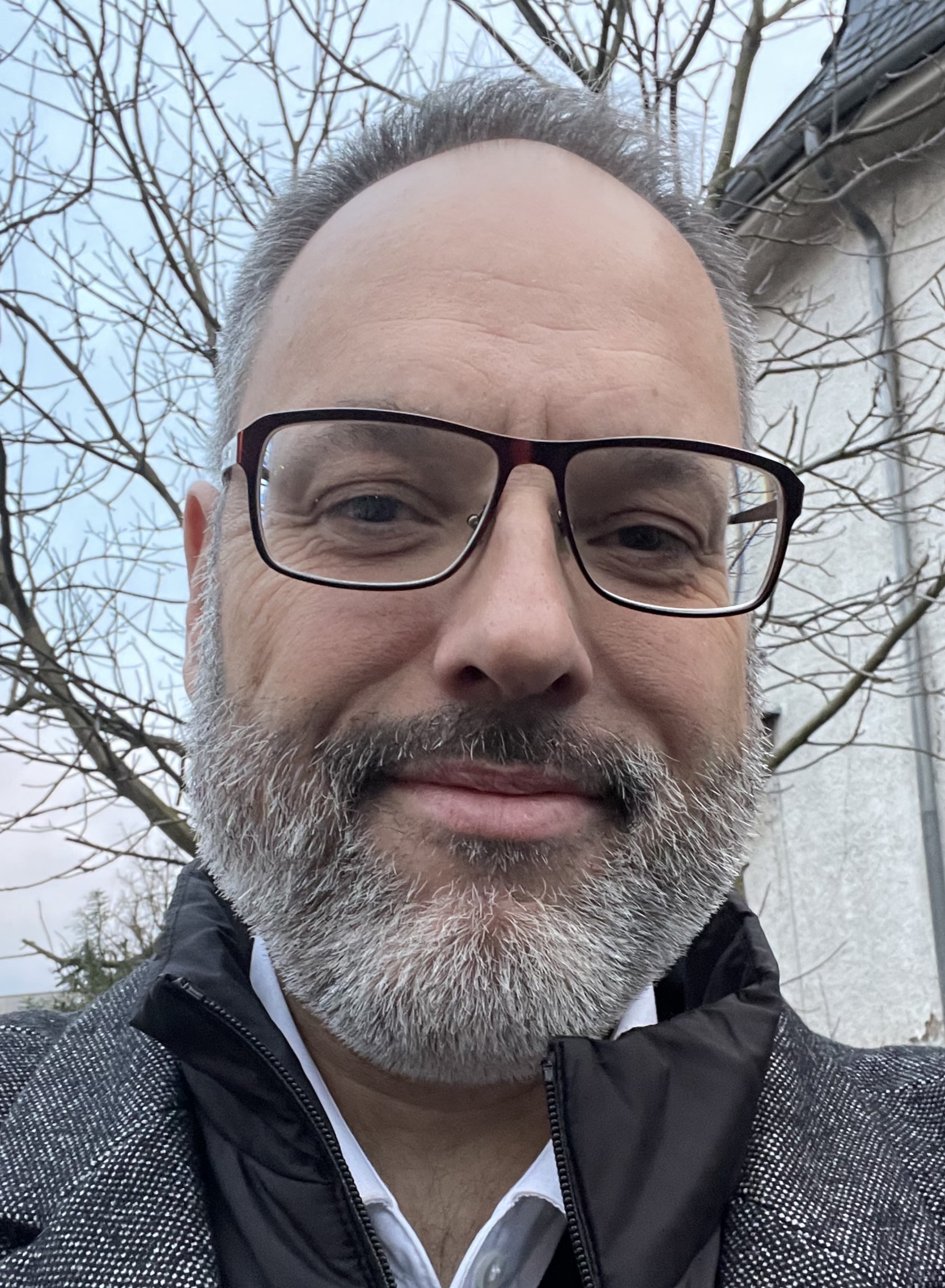 Pfarrer Philip Horn, mit hoher Stirn, ergrauten Haupthaar und Vollbart, dunkler Brille, lächelt in die Kamera.