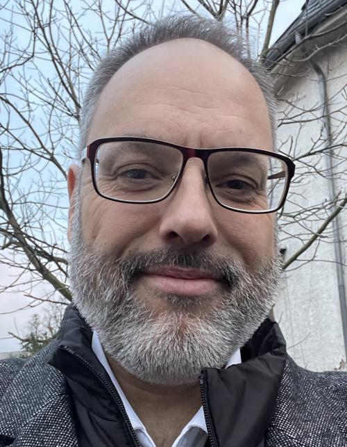 Pfarrer Philip Horn, mit hoher Stirn, ergrauten Haupthaar und Vollbart, dunkler Brille, lächelt in die Kamera.