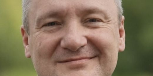 Pfarrer Konrad Lisowski, ein Mann mit leicht ergrauten, kurzen Haaren, die sich im Stirnbereich lichten, blickt verschmitzt in die Kamera.