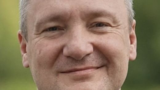 Pfarrer Konrad Lisowski, ein Mann mit leicht ergrauten, kurzen Haaren, die sich im Stirnbereich lichten, blickt verschmitzt in die Kamera.