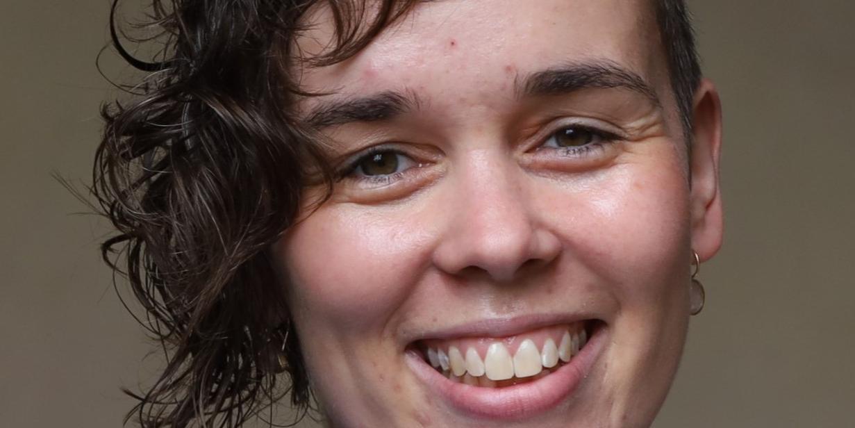 (c) Hannah Theus Eine junge Frau mit einem ovalen Gesicht und dunkelbraunen Haaren, auf ihrer rechten Seite lang, auf der anderen kurzgeschnitten, strahlt Sie an.