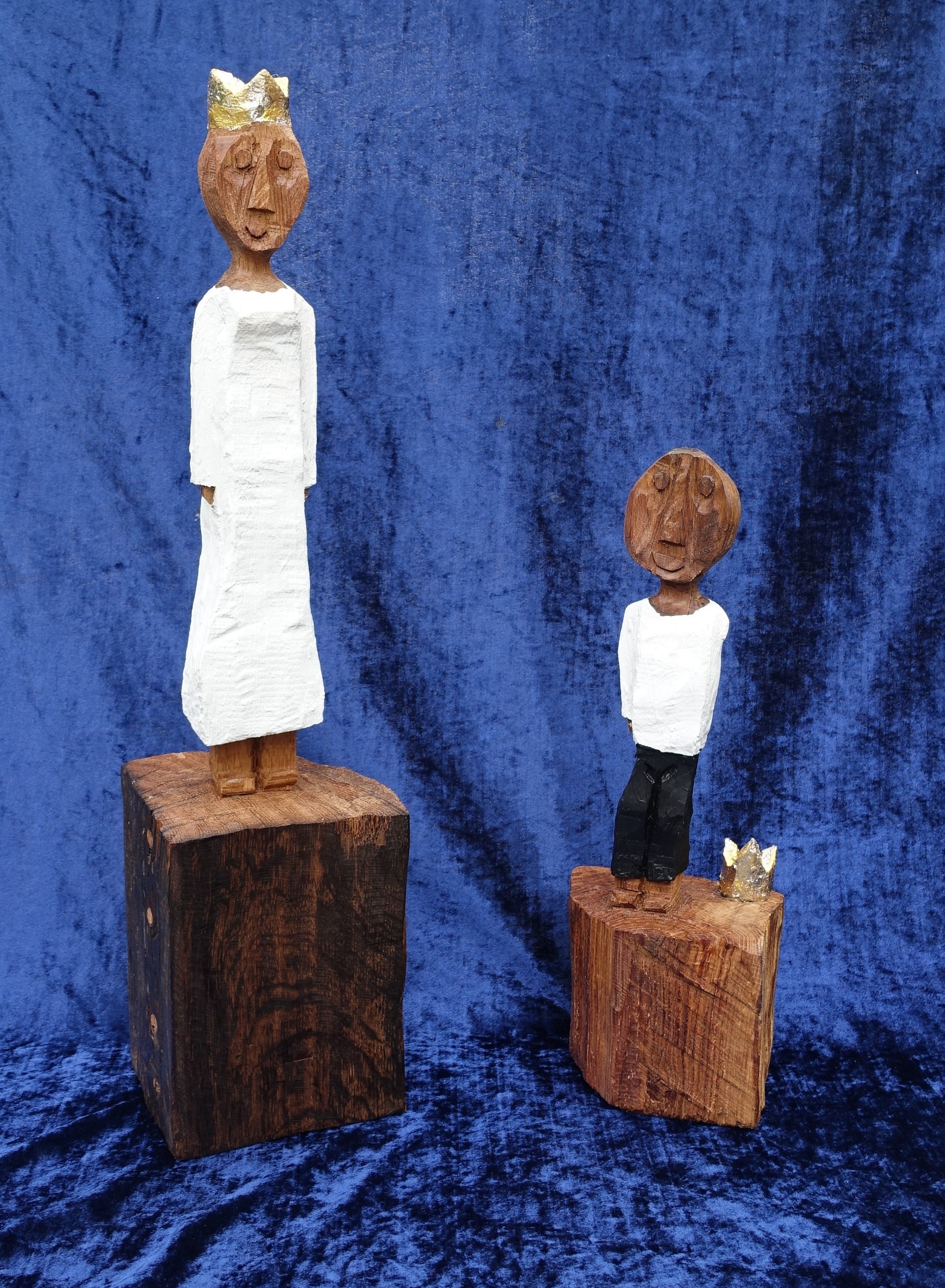 Eine kleinere Königsfigur, mit fehlendem linken Arm - die Krone liegt neben ihm, und eine größere weibliche gekrönte Königsfigur stehen auf schimmerndem blauen Stoff.