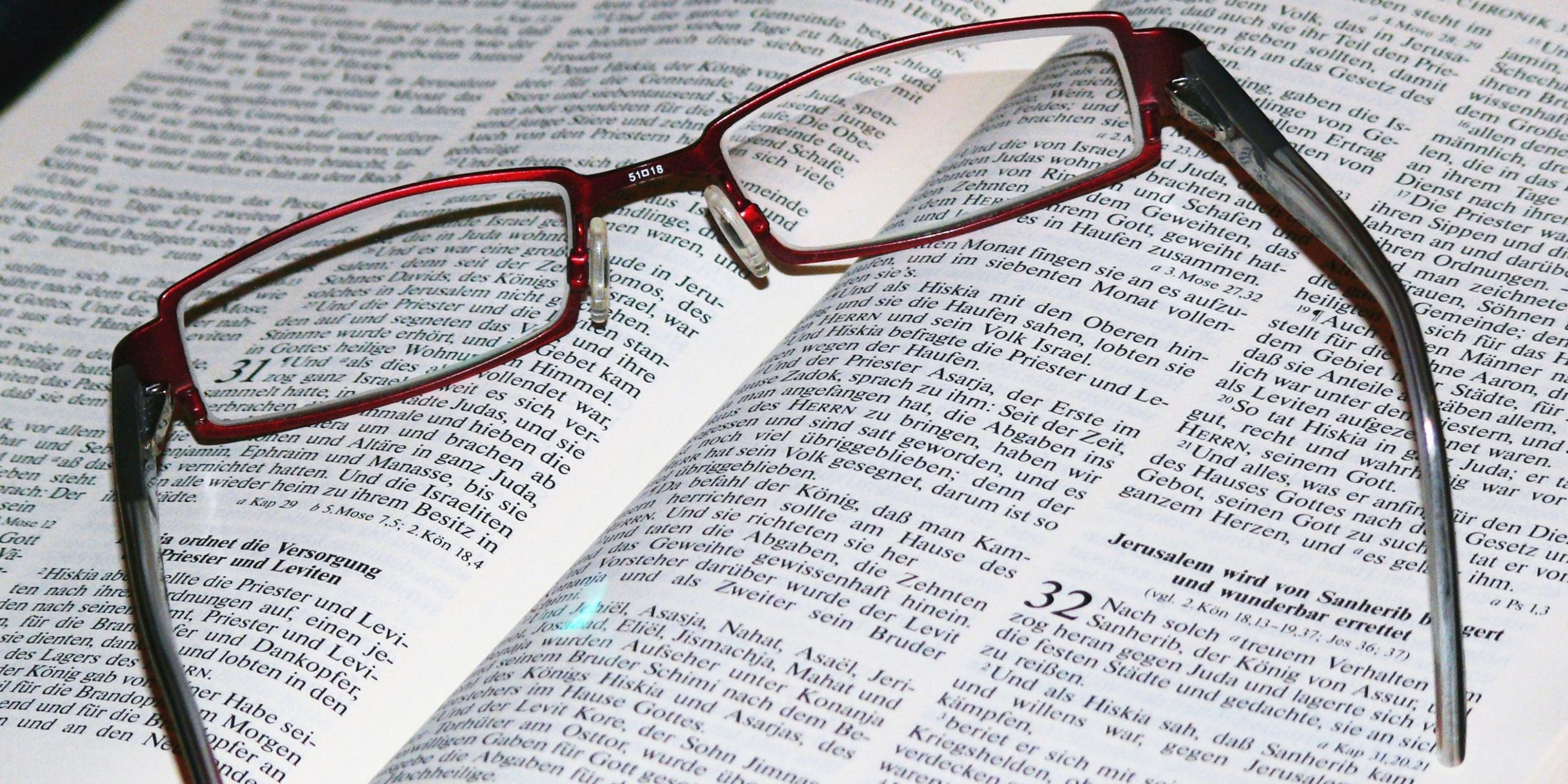 Auf einer aufgeschlagenen Bibel, Bibelstelle: Chronik 32, liegt eine dunkelrote Lesebrille.