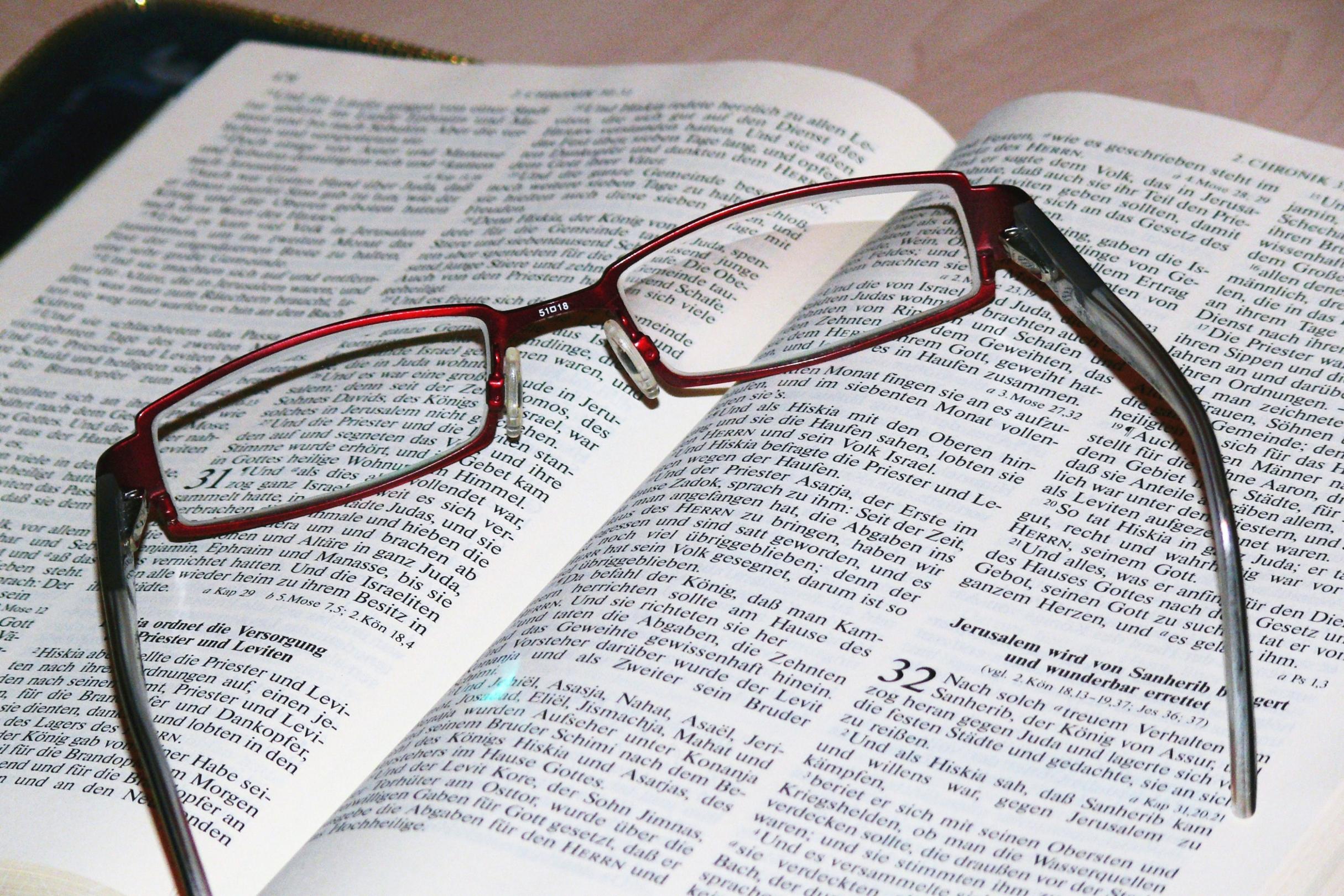 Auf einer aufgeschlagenen Bibel, Bibelstelle: Chronik 32, liegt eine dunkelrote Lesebrille.
