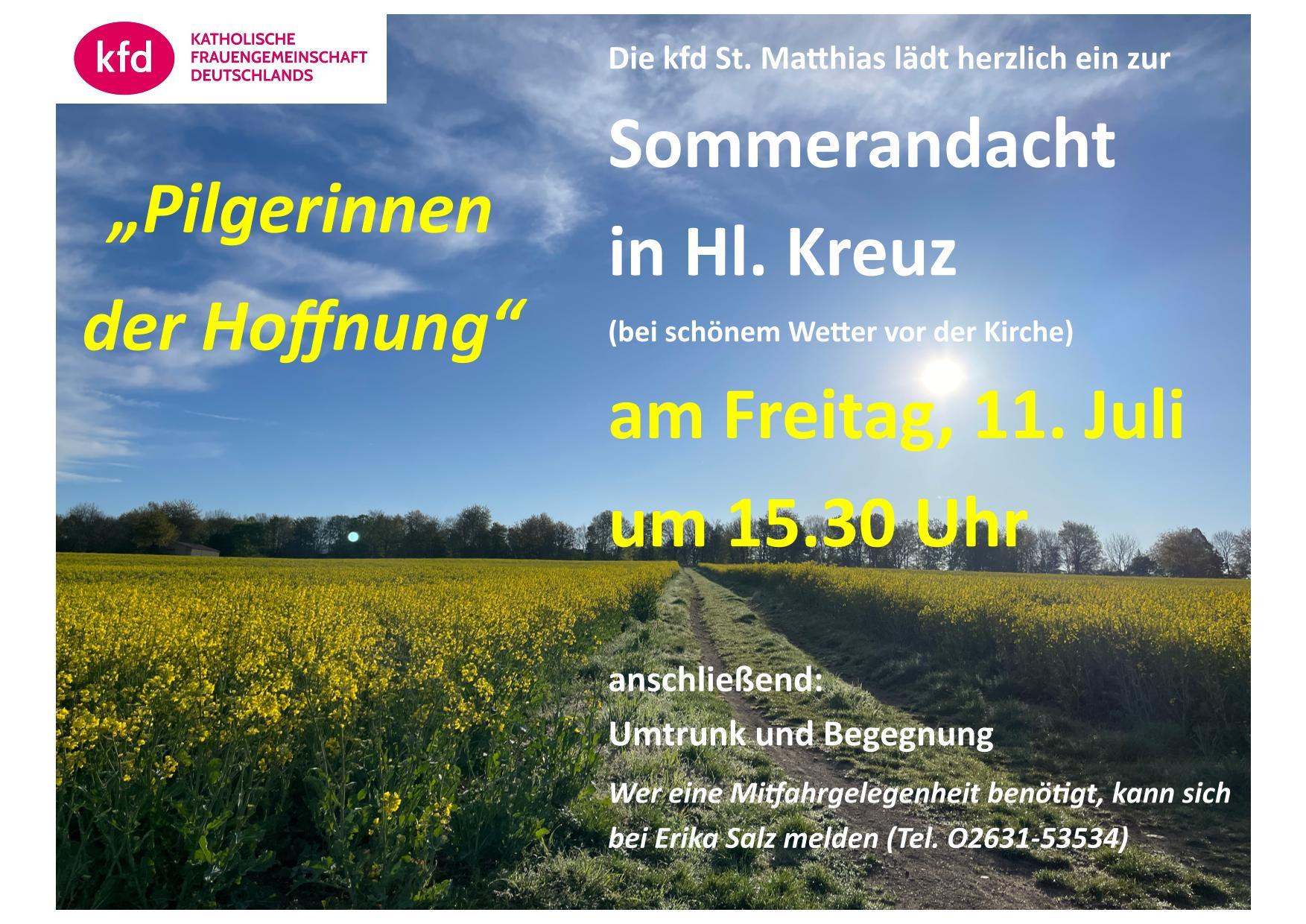 Ein grasbewachsener Feldweg führt durch Rapsfelder auf einen baumbestandenen Horizont zu, unter blauem Himmel mit leichten Schleierwolken.