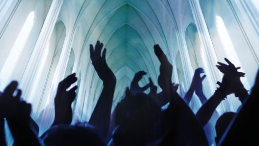 Menschen recken ihre Hände jubelnd und klatschend dem in Blau- und Grüntönen angestrahlten Kirchendeckengewölbe entgegen.