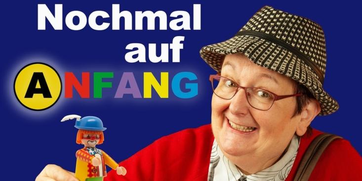 Eine ältere Dame in roter Jacke und Pepita-Hut sitzt hinter einem Mensch-Ärgere-Dich-Nicht-Brett, das mit unterschiedlichen Playmobilfiguren bestellt ist.