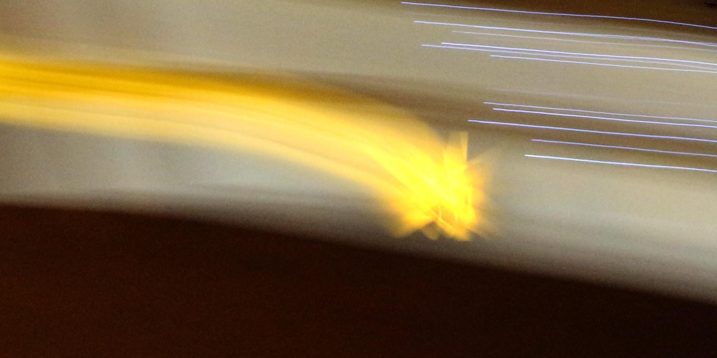 Ein verschwommener gelb-leuchtender Stern mit Schweif auf der linken Seite vor dunklem Hintergrund.