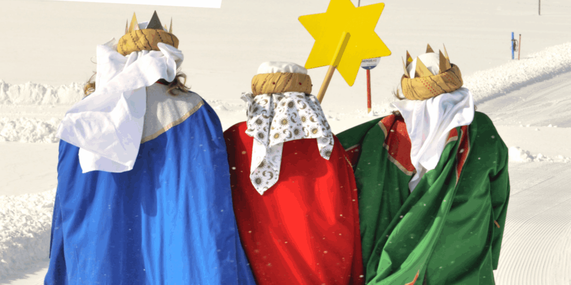 Drei Sternsinger*innen - von hinten zu sehen, in blauem, rotem und grünem Gewand - stapfen durch den Schnee.