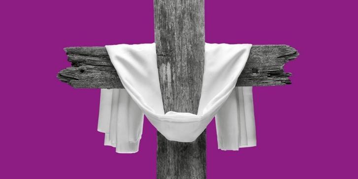 Ein schlichtes, aus alten Bahnschwellen gebautes Kreuz ist mit einem weißen Leinentuch dekoriert, vor violettem Hintergrund.