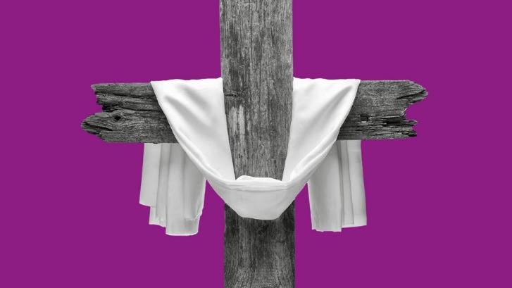 Ein schlichtes, aus alten Bahnschwellen gebautes Kreuz ist mit einem weißen Leinentuch dekoriert, vor violettem Hintergrund.