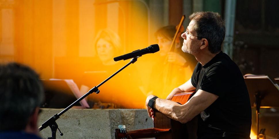 Gregor Linßen sitzt an einem Altar, die Gitarre auf dem Schoß, nachdenklich zum Mikro schauend.