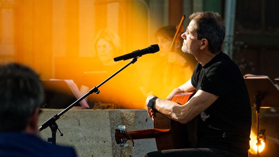 Gregor Linßen sitzt an einem Altar, die Gitarre auf dem Schoß, nachdenklich zum Mikro schauend.