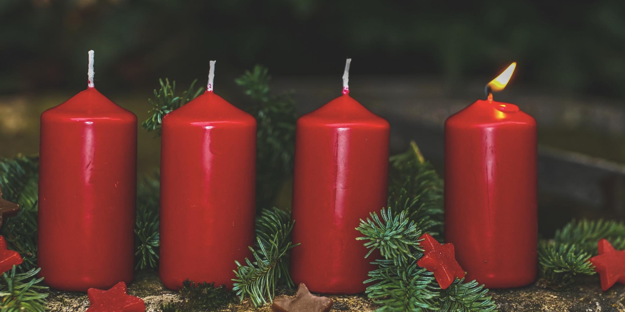 Kirchenmusik in Dierdorf: 1. Adventssonntag 2026 Das Bild zeigt vier rote Adventskerzen, die mit Tannenzweigen und kleinen roten Sternen dekoriert sind. Die erste Kerze, ganz rechts, brennt.