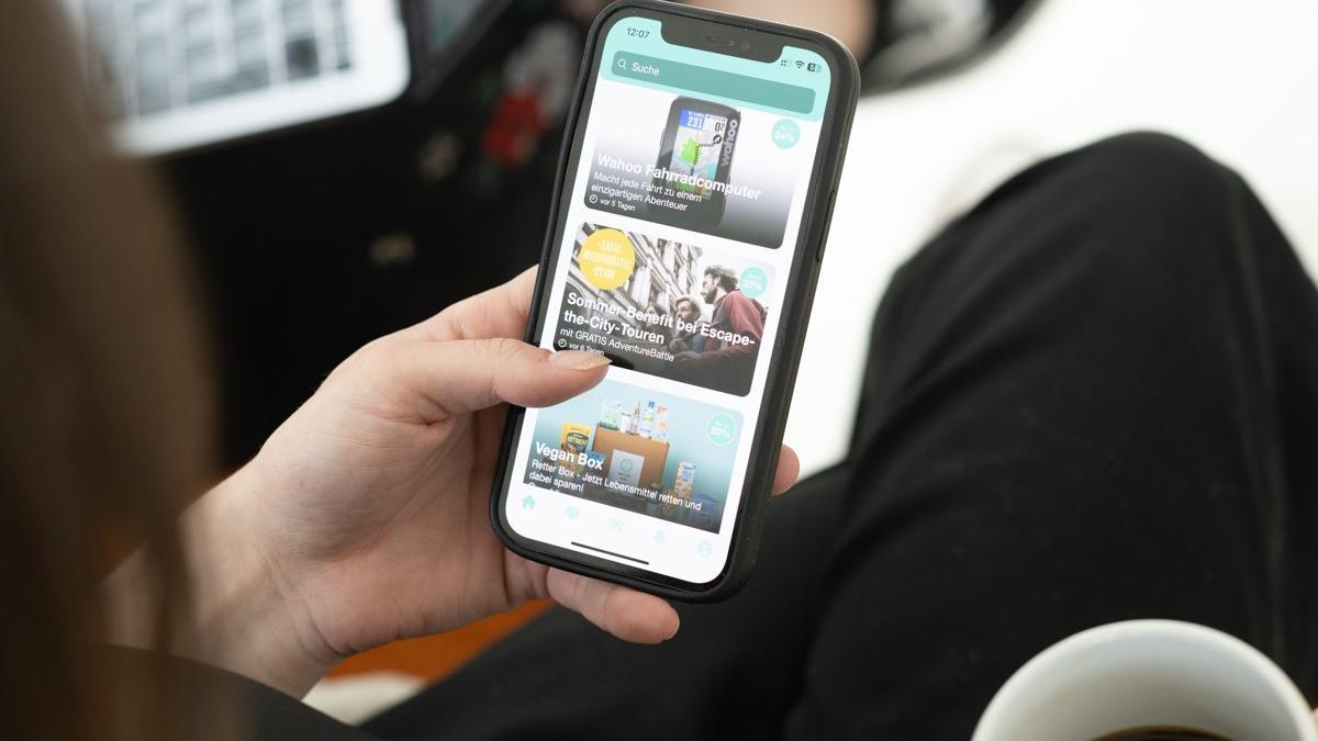 Eine linke Hand hält ein Smartphone, auf dem die App 'benefits.me' aufgerufen ist.
